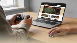 A hand of a video gamer holding a joystick in front of a laptop with casino website on the screen and casino chips on the side